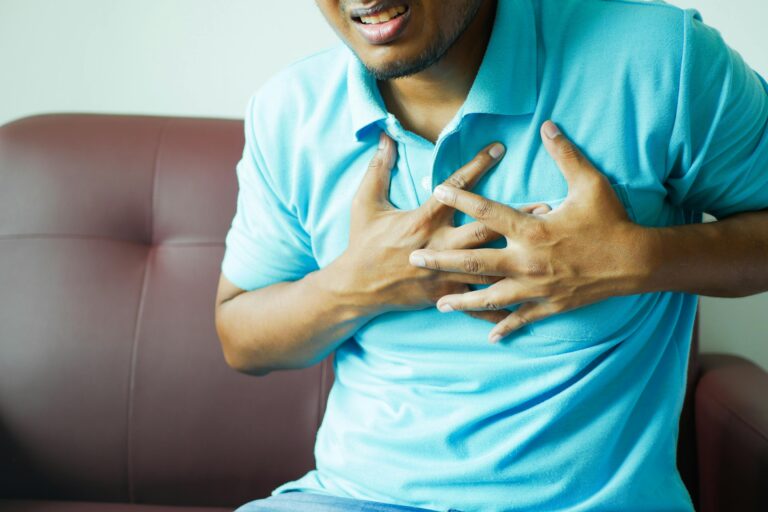 A close-up image of a man clutching his chest, indicating heart pain or discomfort.